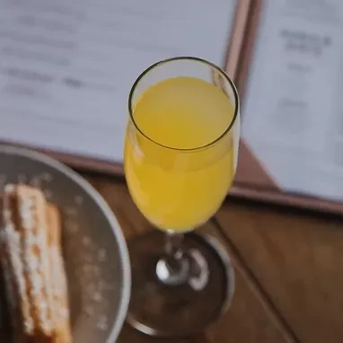 Close-up: Flute glass with orange drink, sugared pastry on wood.