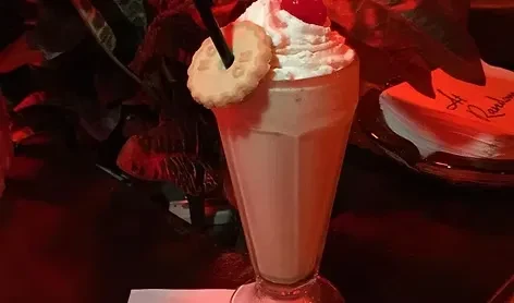 Red-lit milkshake with whipped cream, cherry, straw, and a biscuit.