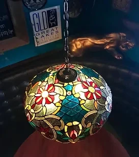 Vibrant stained-glass lamp with floral patterns illuminates a dim distillery interior.