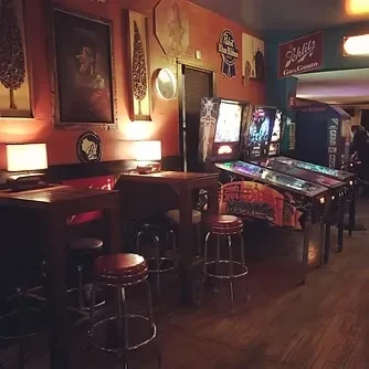 Dimly lit retro bar with vibrant pinball machines and rustic tables.