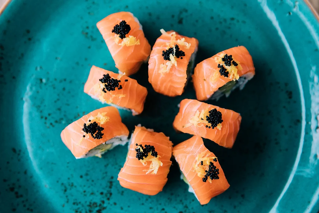 Eight salmon maki rolls with caviar and zest on a teal plate.