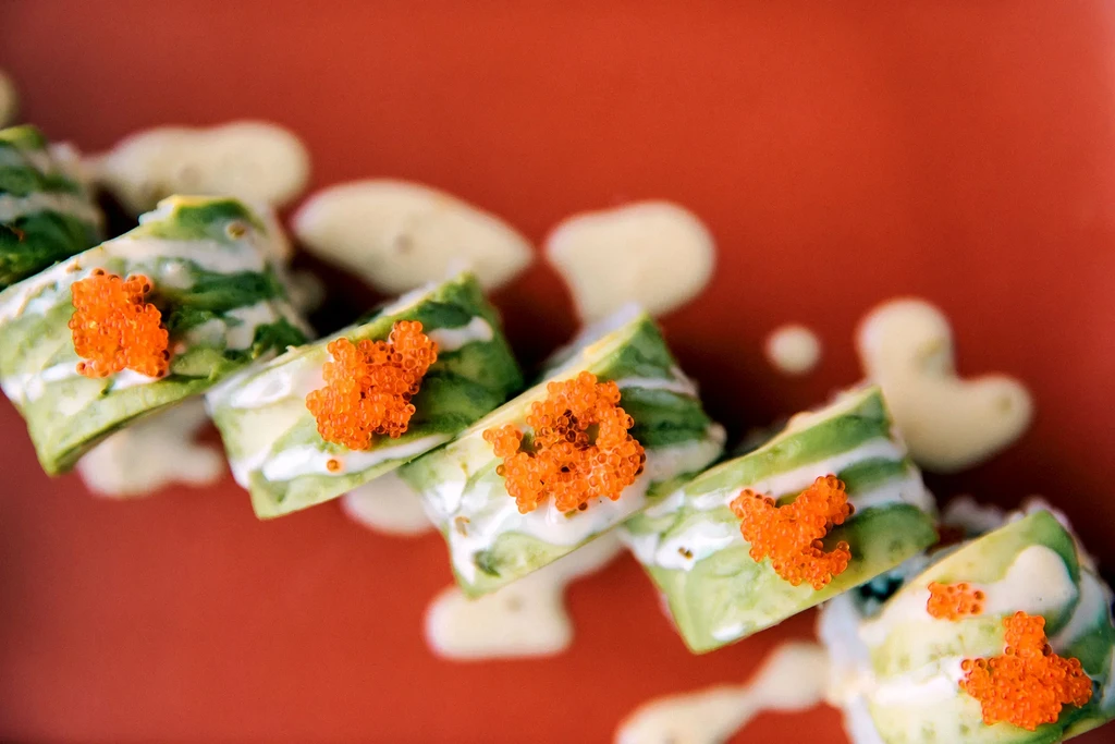 Sushi rolls with avocado, orange roe, white sauce on red plate.