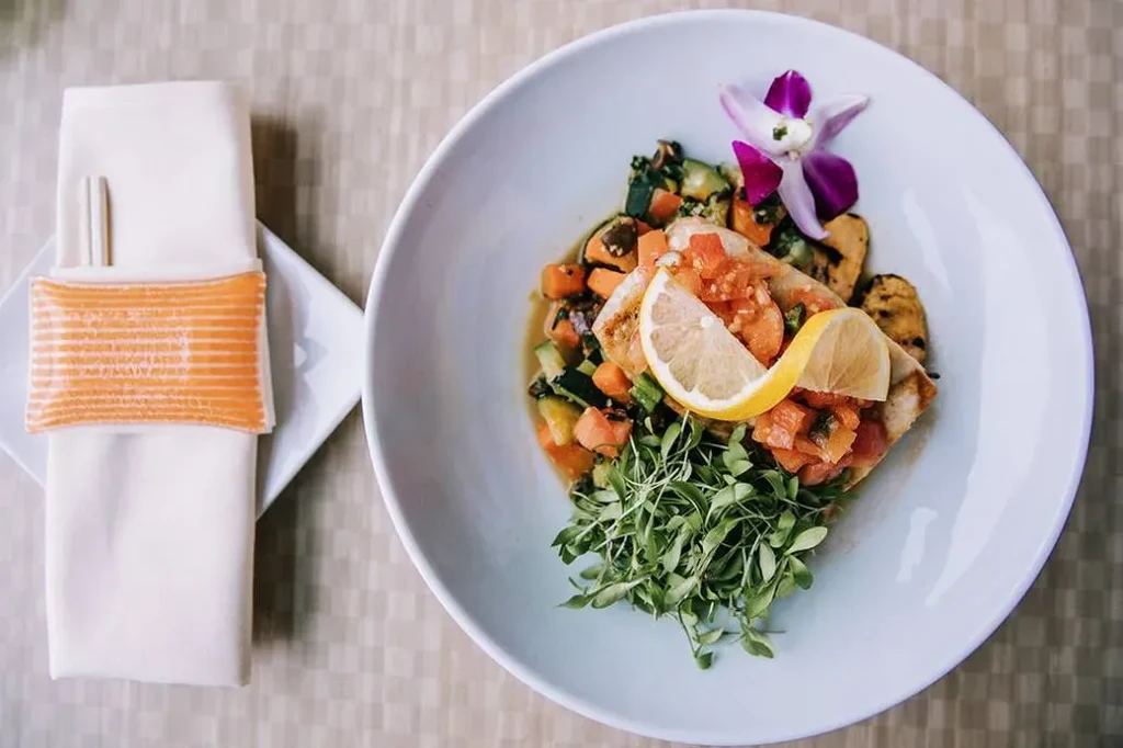 Pan-seared fish with tomato salsa, vegetables, orchid garnish, and chopsticks.