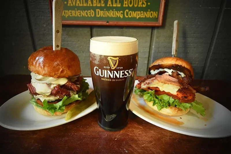 Guinness stout and two gourmet burgers on a dark pub table.