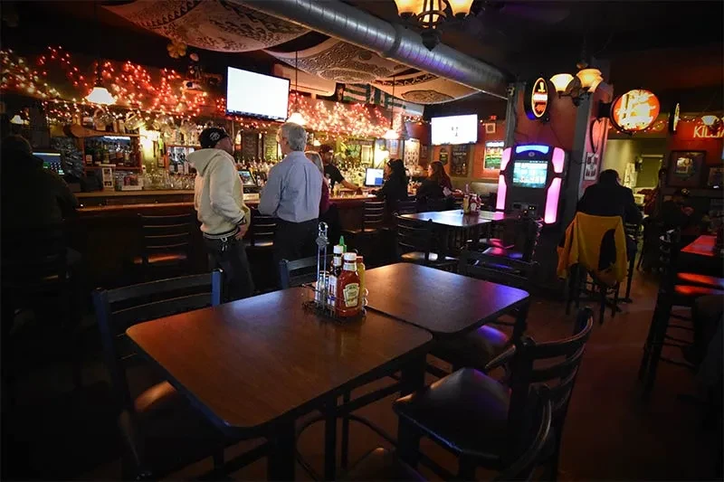 Dimly lit bar interior, patrons, well-stocked counter, and illuminated jukebox.
