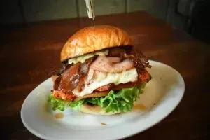 Stacked burger with lettuce, patty, melted cheese, and bacon on a plate.