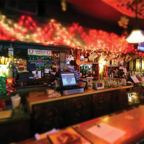 Rustic bar interior with liquor bottles, menu, and red string lights.