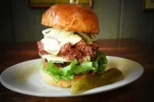 Pulled meat burger on brioche bun with cheese and pickle spear.