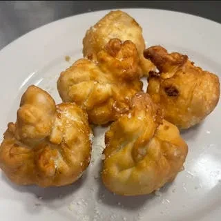 Five golden-brown fritters on a white plate, dusted with white powder.