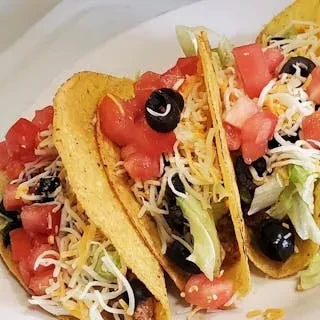 Three crispy tacos filled with lettuce, tomato, cheese, and olives.