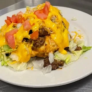 Taco salad piled high with meat, melted cheese, tomatoes, and lettuce.