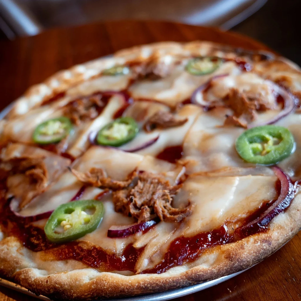 Golden-brown barbecue pulled meat pizza with cheese, jalapeños, onions.