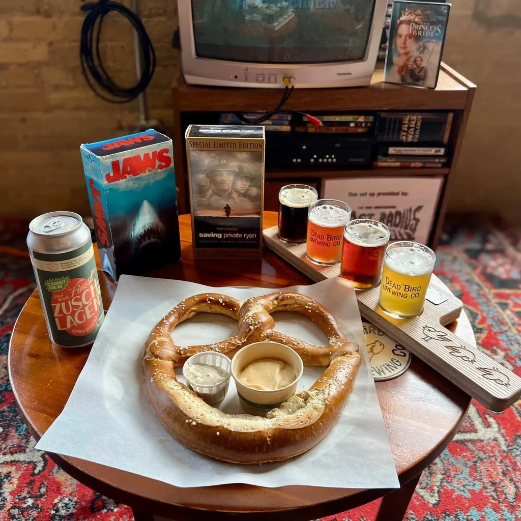 A salted pretzel, beer flight, lager, and retro TV with VHS.