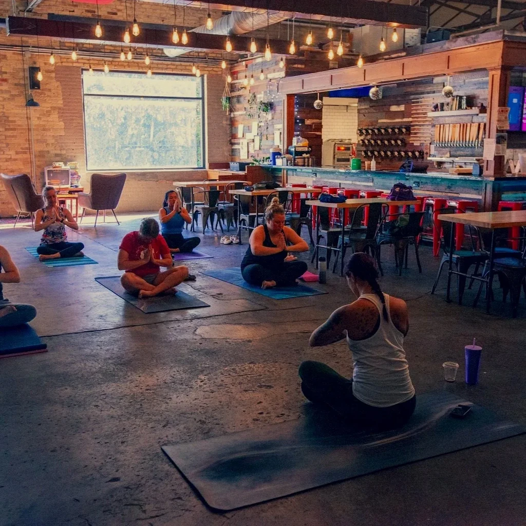 Group meditating in a rustic brewery with Edison bulbs and beer taps.