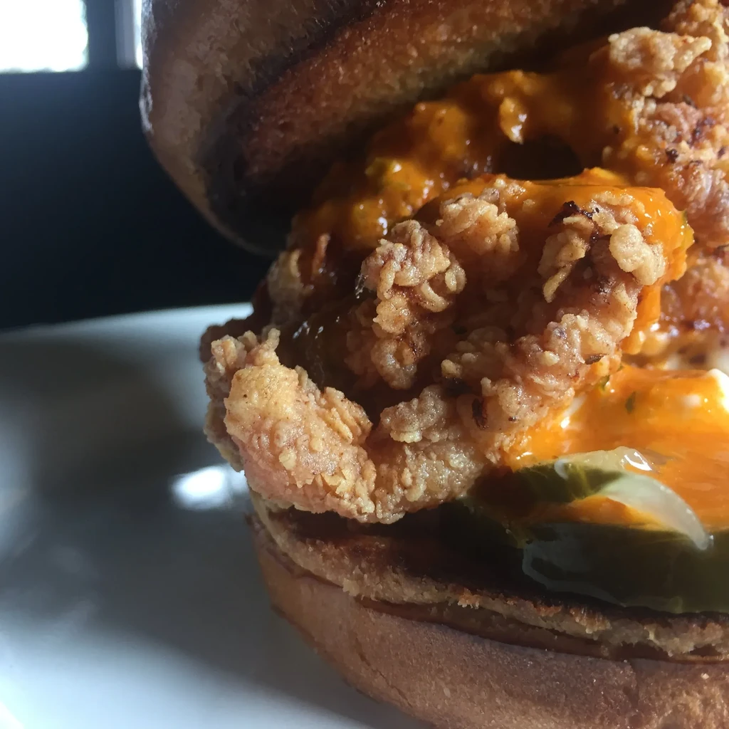 Close-up: crispy fried chicken sandwich with orange sauce and pickles.
