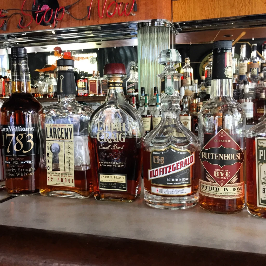Whiskey and bourbon bottles, including Larceny and Elijah Craig, on a bar.