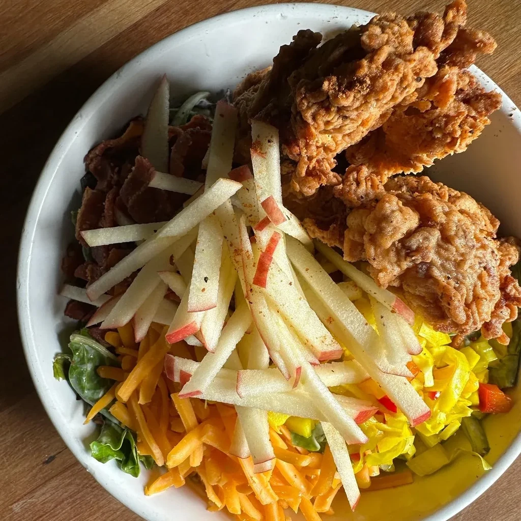 Fried chicken and vibrant apple-carrot salad in a white bowl.
