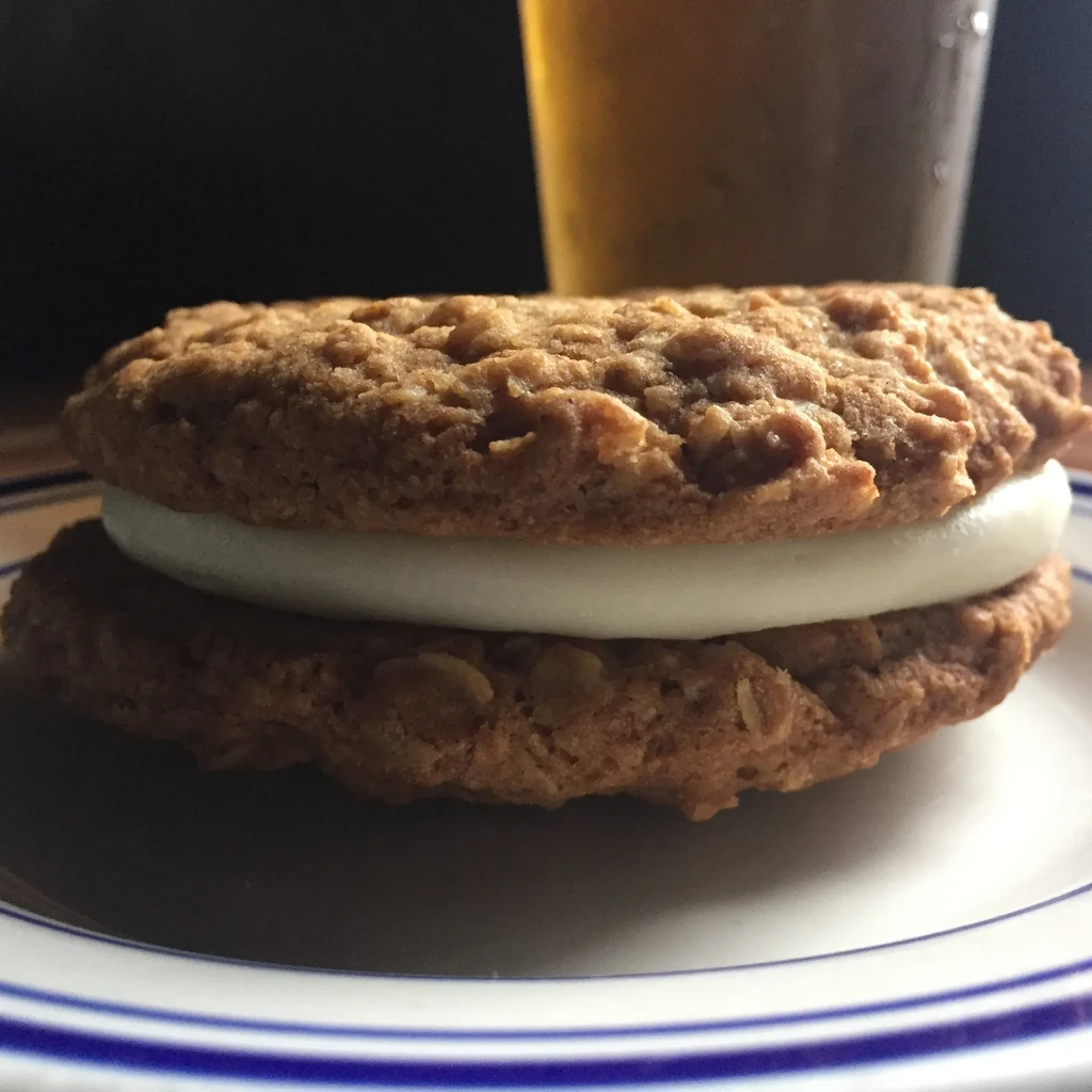 Single oat-speckled sandwich cookie with creamy white filling on a striped plate.