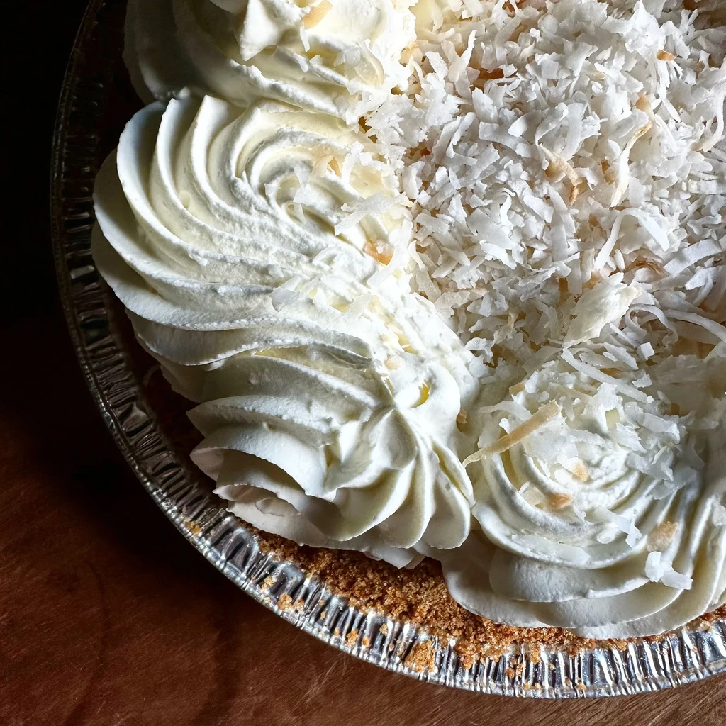Overhead: Coconut cream pie with whipped cream, toasted coconut, graham crust.