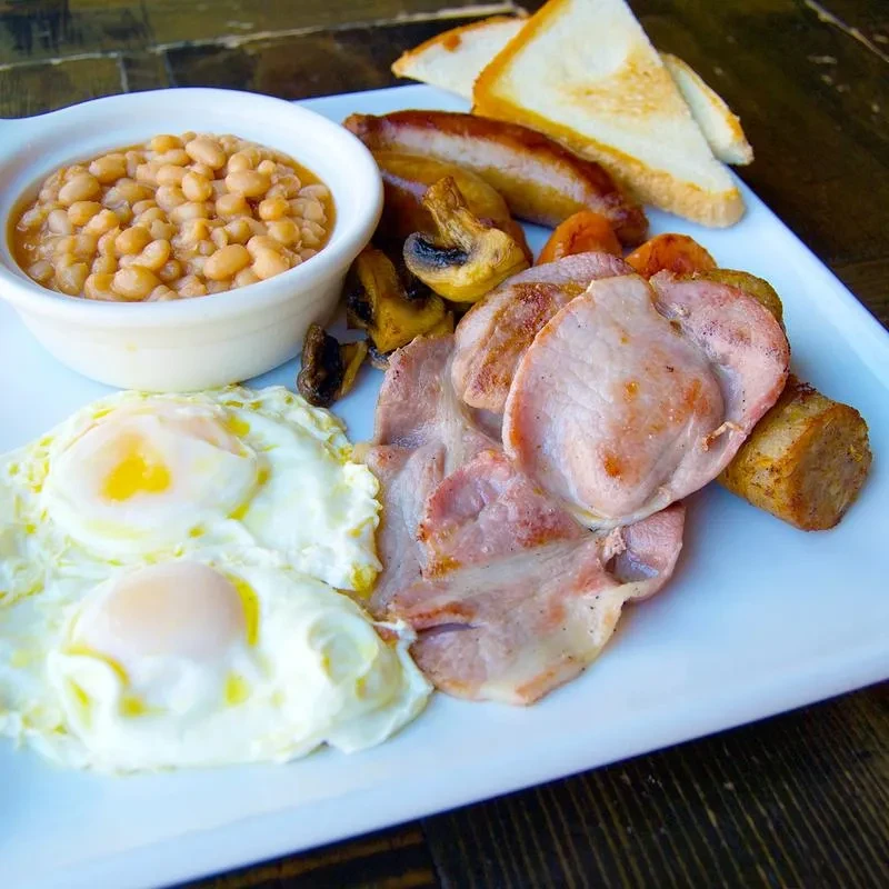 Classic full English breakfast with eggs, bacon, sausage, beans, mushrooms, and toast.