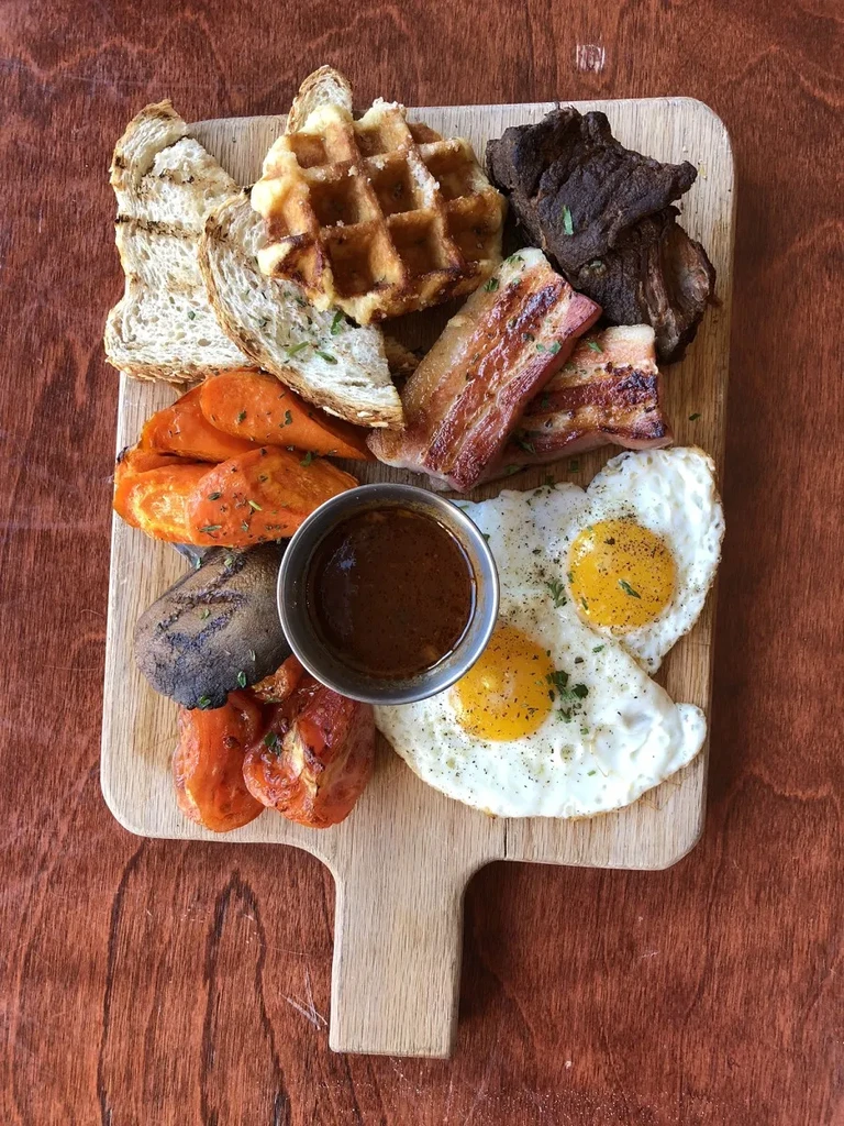 Breakfast platter with eggs, bacon, waffle, toast, and roasted vegetables.