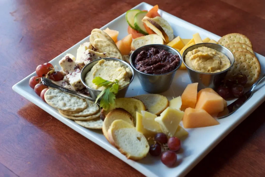 Charcuterie board with cheeses, grapes, melon, crackers, and dips.