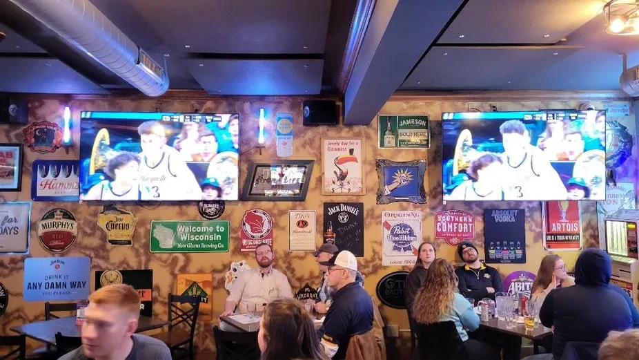 Sports bar interior: vintage signs, basketball on TVs, and people seated.