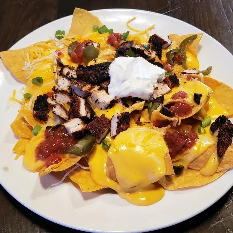 Close-up of loaded chicken nachos with cheese sauce, salsa, sour cream.