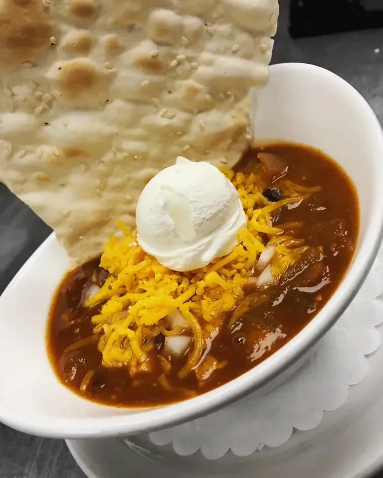 Reddish-brown chili with cheese, onions, sour cream, and sesame flatbread.