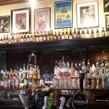 Bar interior: many liquor bottles, beer taps, and a Beatles poster.