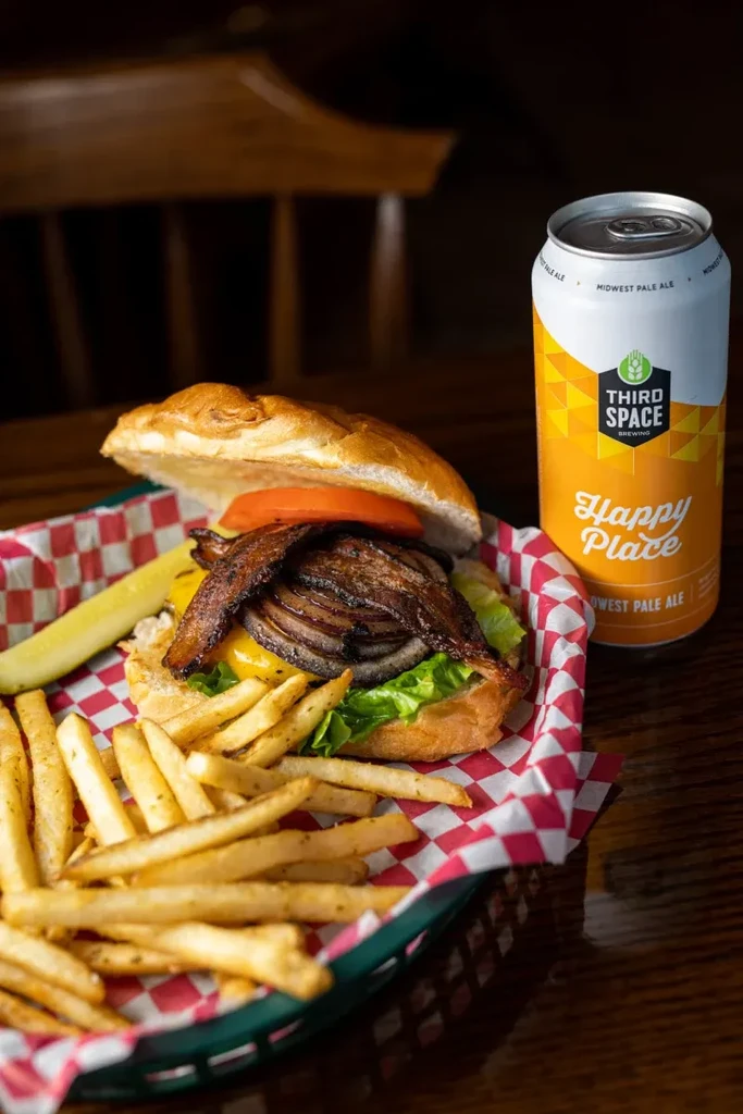Open-faced burger with fries, pickle, and craft beer on a wooden table.