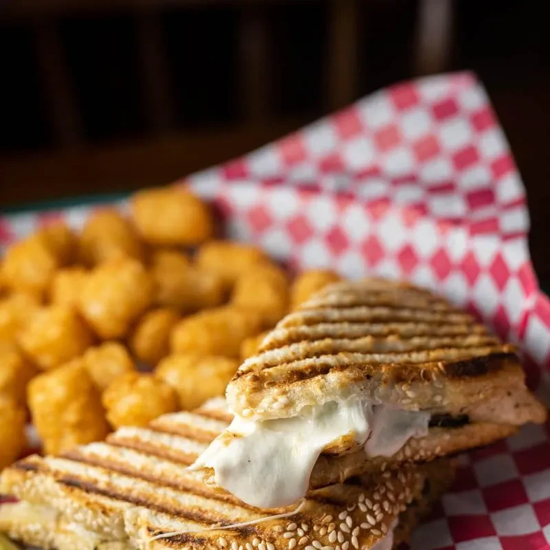 Grilled sandwich with oozing melted cheese, sesame seeds, and tater tots.