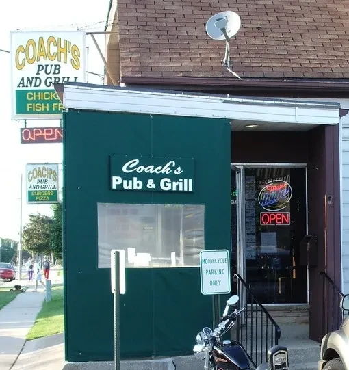 Coach's Pub & Grill exterior, green awning, pole sign, and parked motorcycle.
