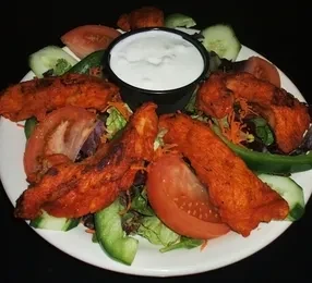 Brightly seasoned chicken strips on lettuce with tomatoes, cucumber, and dip.