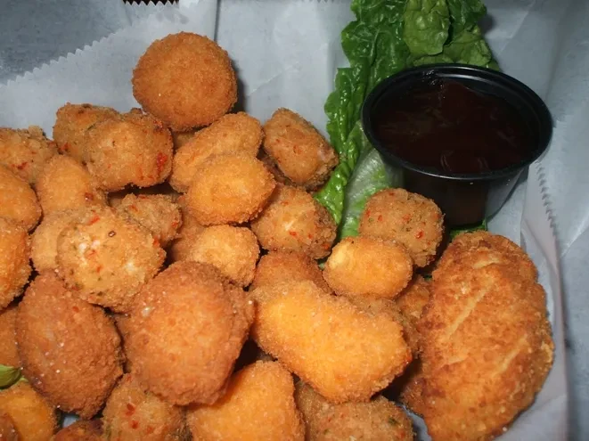 Crispy golden-brown fried bites with chili flakes, lettuce, and dipping sauce.