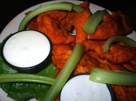 Plate of saucy Buffalo chicken wings, celery, and two white dips.