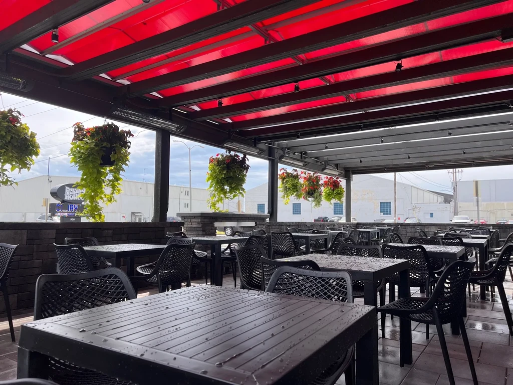 Outdoor patio with dark wet tables, red awning, hanging plants.