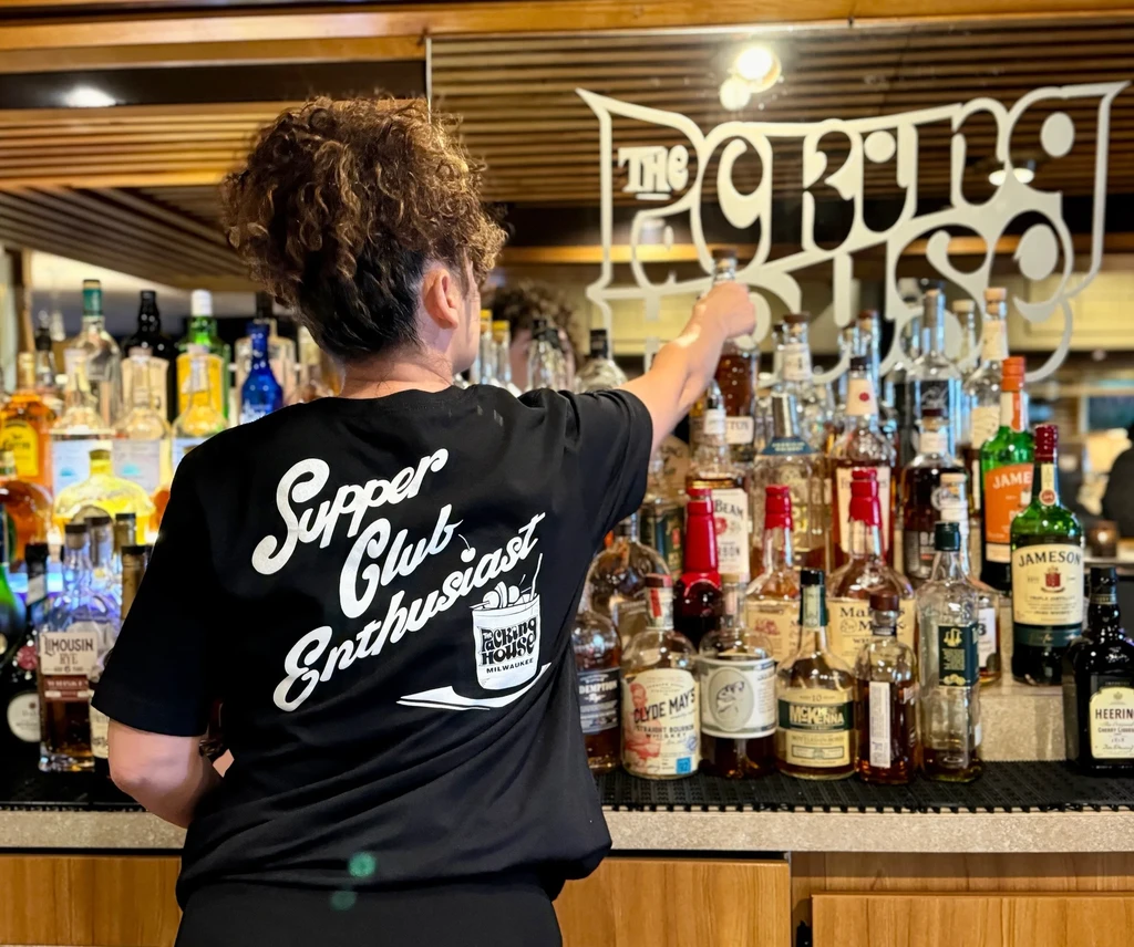 Bartender at The Packing House reaches for bottle behind well-stocked bar.