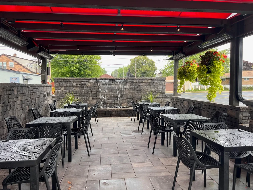 Empty outdoor restaurant patio, black tables, red awning, water feature.