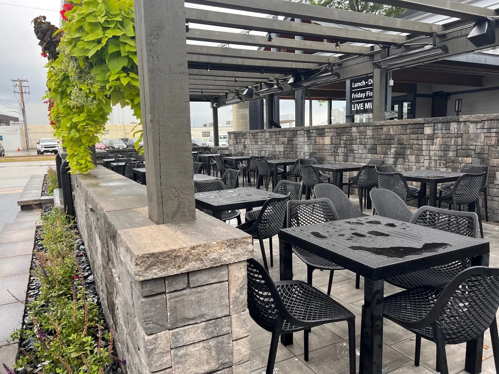 Empty outdoor restaurant patio with wet tables under a pergola.