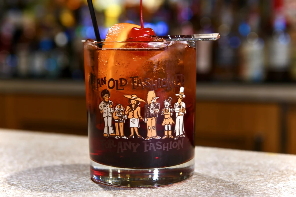 Amber cocktail with orange, cherry in an illustrated Old Fashioned glass.