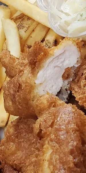 Close-up of golden fried chicken, french fries, and white sauce.