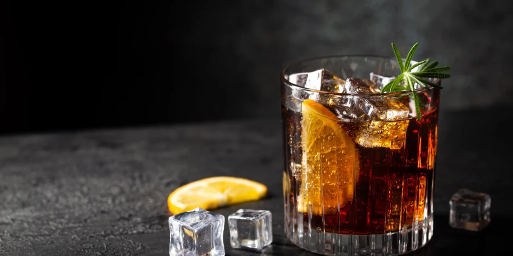 Dark beverage in ribbed glass with ice, orange, and rosemary.