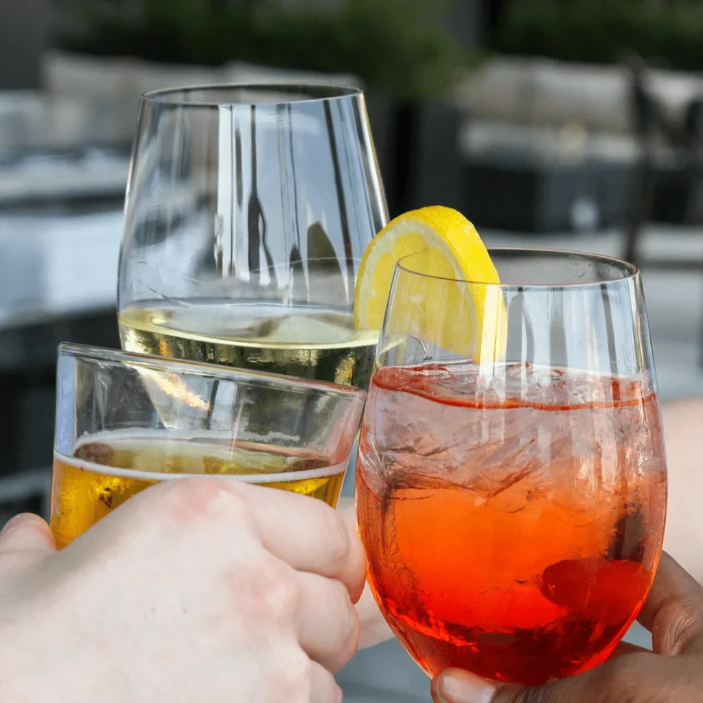 Three hands toasting with beer, white wine, and an orange cocktail.