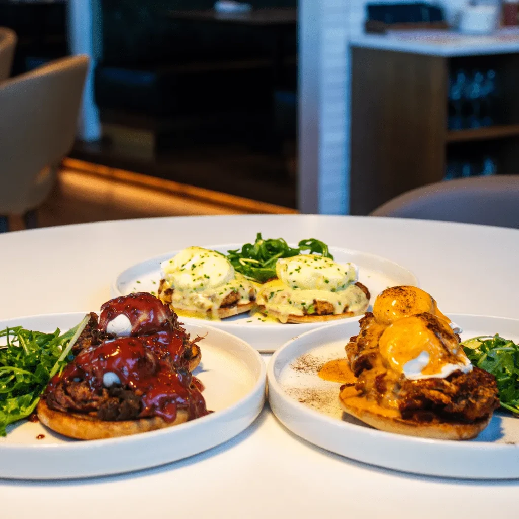 Three different Eggs Benedict dishes with sauces in a restaurant setting.