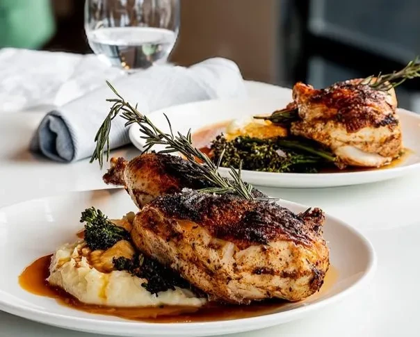 Crispy roasted chicken with mashed potatoes, greens, and dark sauce on plates.