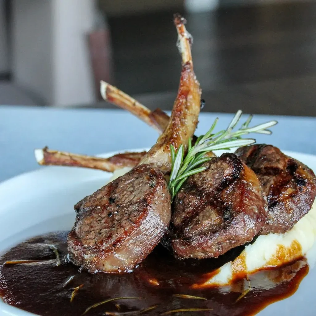 Grilled lamb chops, mashed potatoes, dark sauce, and rosemary garnish.