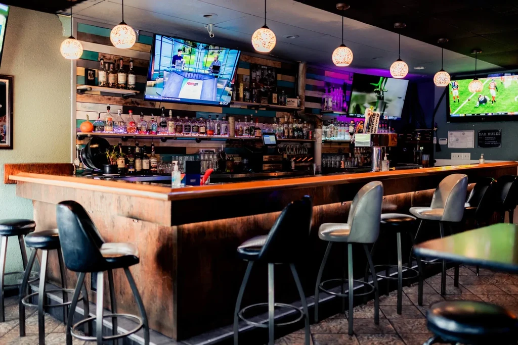 Sports bar interior with wooden counter, liquor bottles, and TVs showing sports.