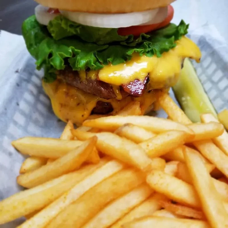 Close-up: A double-patty cheeseburger with bacon, fries, and pickle.