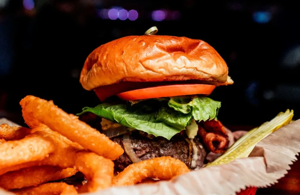Gourmet burger with melted cheese, crispy bacon, fries, and dill pickle.